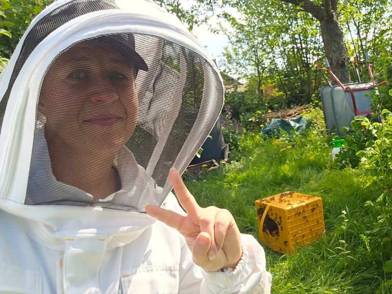 Imkerin im Schutzanzug vor den Bienenstöcken im Garten